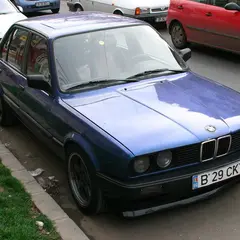 Restored blue BMW E30 sedan, front three-quarter view with black BBS-style wheels