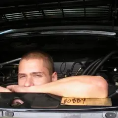 Young mechanic leaning into the open engine bay of an air-cooled Porsche 911 in the workshop